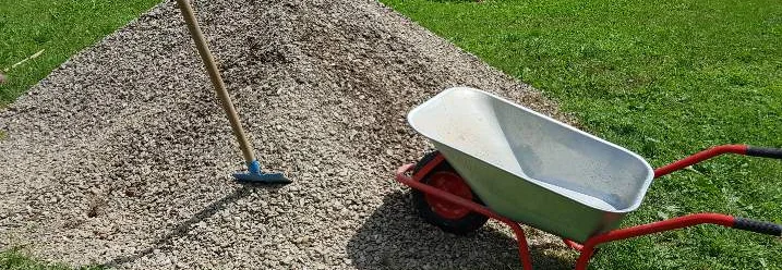 Kieshaufen und Schubkarre auf Rasen